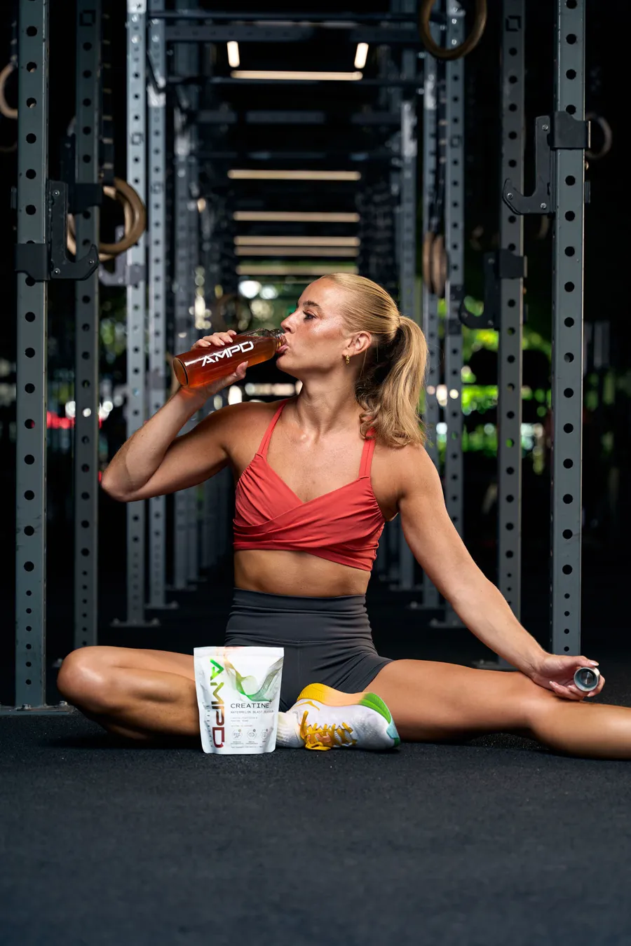 Athlete stretching in the gym drinking AMPD, Creatine+ pouch beside her