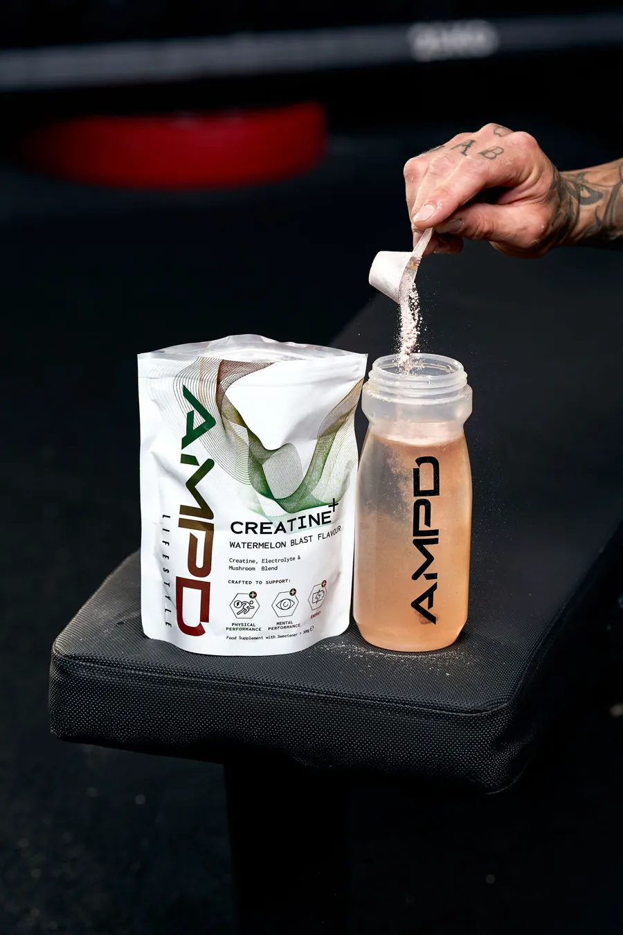 A scoop of Creatine+ being poured into an AMPD bottle next to the pouch